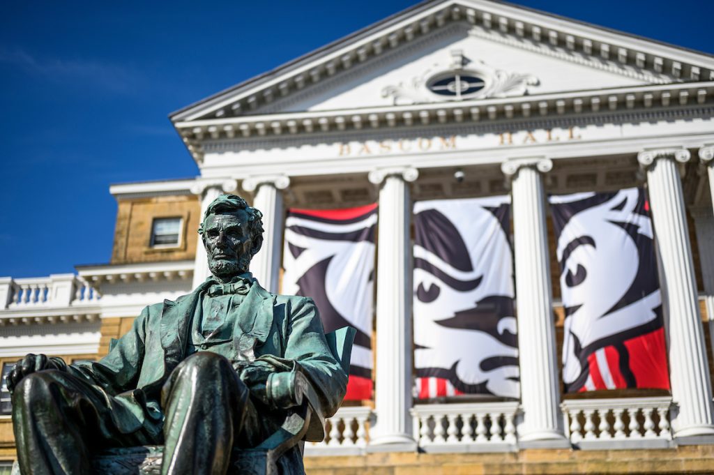 Abraham Lincoln statue in front of Bascom Hill with Bucky Badger banners positioned between columns.